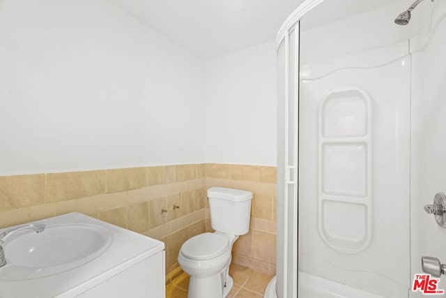 bathroom with toilet, a shower, tile walls, and tile patterned floors