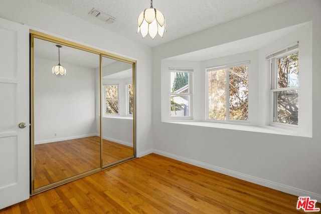 unfurnished bedroom with a textured ceiling, a closet, hardwood / wood-style floors, and a notable chandelier