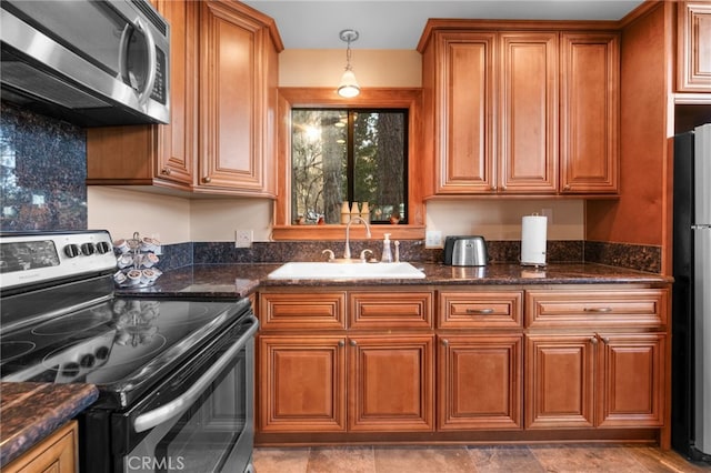 kitchen with decorative light fixtures, sink, stainless steel appliances, and dark stone counters