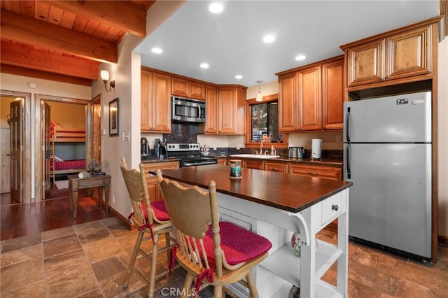 kitchen with beam ceiling, sink, decorative light fixtures, a kitchen island, and appliances with stainless steel finishes