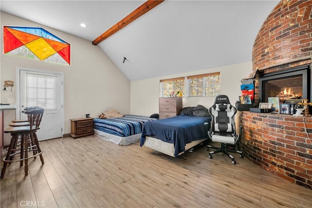 bedroom featuring hardwood / wood-style floors, lofted ceiling with beams, a brick fireplace, and multiple windows