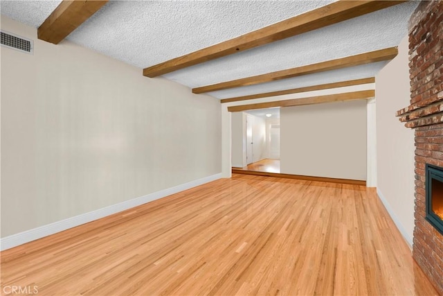 unfurnished living room featuring a fireplace, beam ceiling, light wood-type flooring, and a textured ceiling