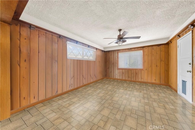 unfurnished room with ceiling fan, wood walls, and a textured ceiling