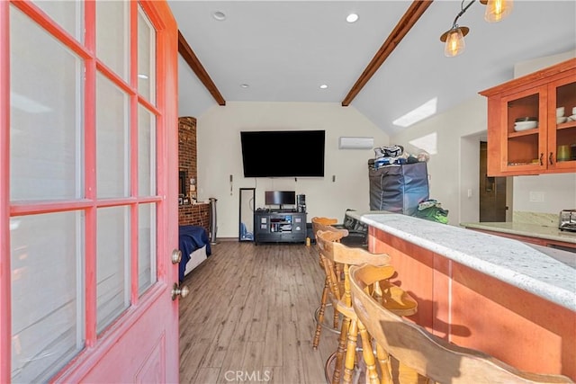 kitchen featuring a fireplace, light stone counters, light hardwood / wood-style flooring, and lofted ceiling with beams