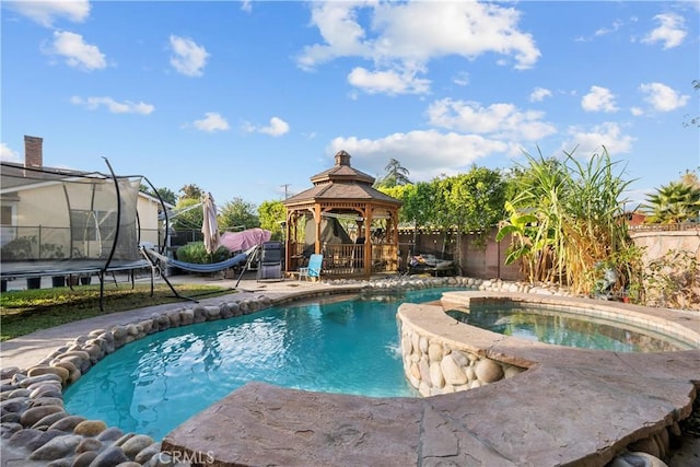 view of swimming pool featuring a gazebo, a trampoline, and an in ground hot tub