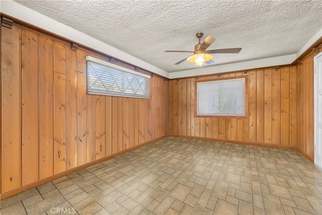 spare room featuring wooden walls, a textured ceiling, and a wealth of natural light