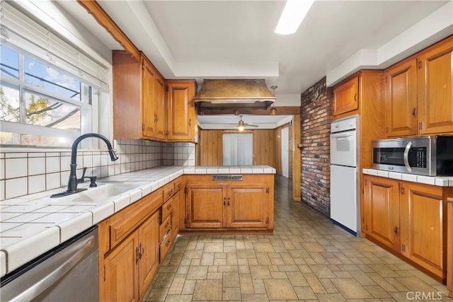 kitchen with kitchen peninsula, stainless steel appliances, ceiling fan, sink, and tile counters