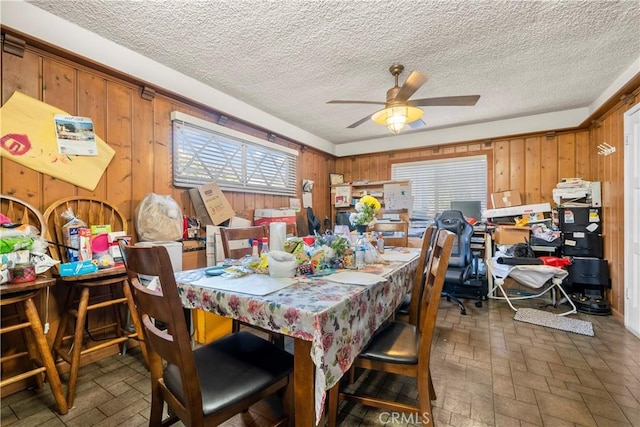 dining area with a textured ceiling, ceiling fan, and wood walls