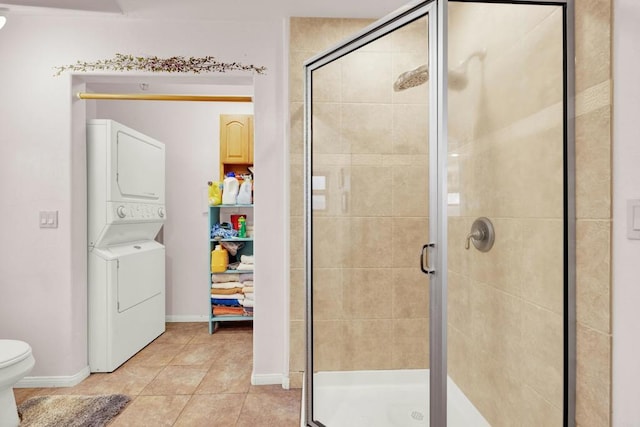 bathroom featuring tile patterned flooring, stacked washing maching and dryer, toilet, and an enclosed shower