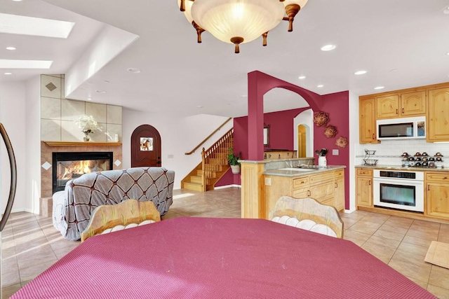 kitchen featuring a tile fireplace, a skylight, light brown cabinets, backsplash, and white appliances