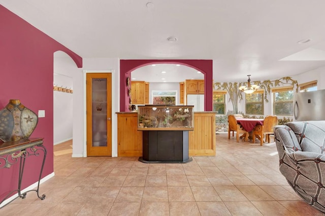 kitchen with kitchen peninsula, stainless steel fridge, light tile patterned floors, and a chandelier