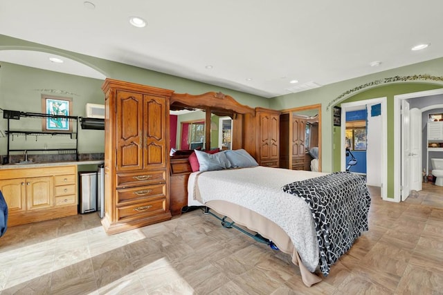 bedroom with stainless steel fridge, sink, connected bathroom, and multiple windows