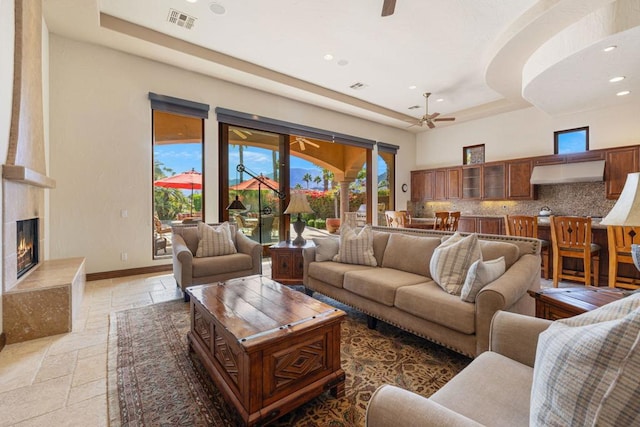 living room with ceiling fan, a large fireplace, and a raised ceiling