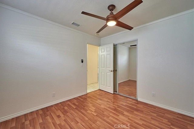 unfurnished bedroom featuring ceiling fan, light wood-type flooring, crown molding, and a closet