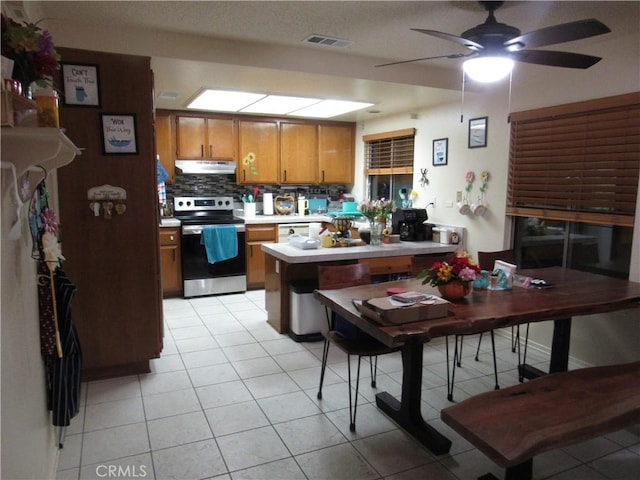 kitchen featuring kitchen peninsula, decorative backsplash, ceiling fan, light tile patterned floors, and stainless steel range with electric cooktop