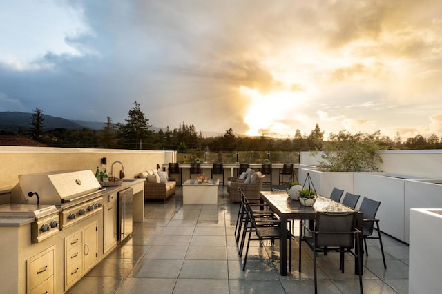 patio terrace at dusk with a grill, exterior kitchen, and sink