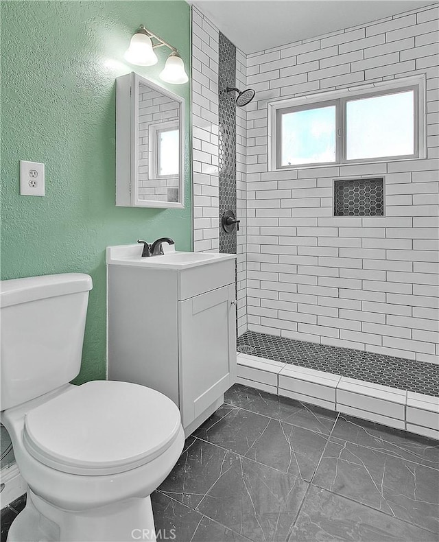 bathroom featuring toilet, vanity, and tiled shower