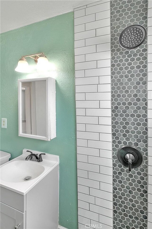 bathroom featuring toilet, vanity, and tiled shower