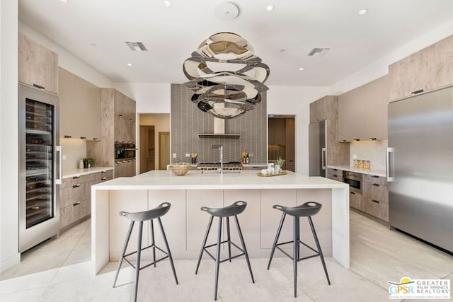 kitchen featuring backsplash, a center island with sink, wine cooler, built in appliances, and a kitchen bar