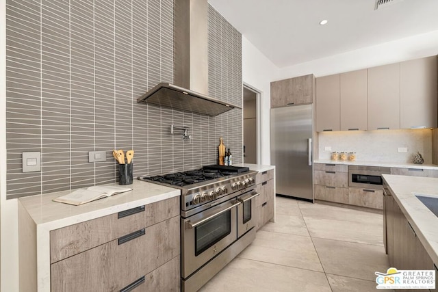 kitchen featuring tasteful backsplash, high quality appliances, wall chimney exhaust hood, and light tile patterned floors