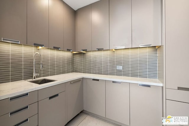 kitchen featuring tasteful backsplash, gray cabinets, light stone countertops, and sink