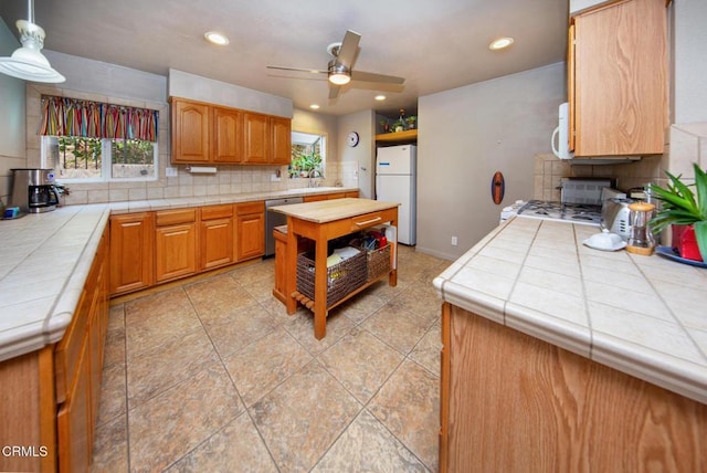 kitchen featuring white appliances, backsplash, sink, ceiling fan, and tile counters