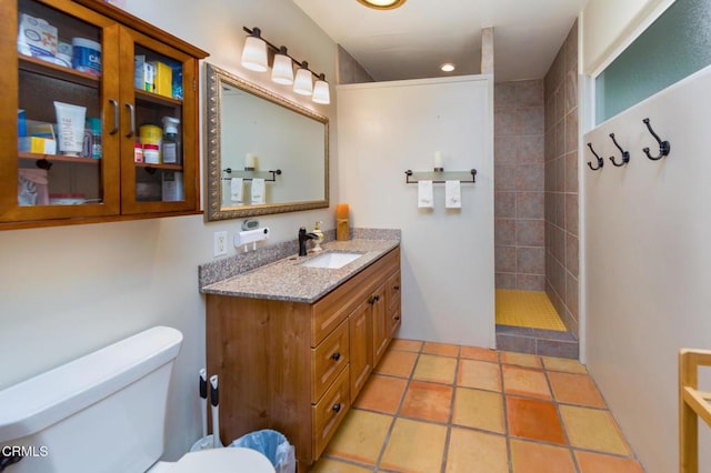 bathroom featuring tile patterned floors, toilet, a tile shower, and vanity