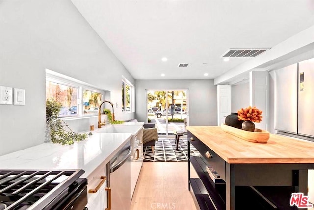 kitchen with sink, light hardwood / wood-style flooring, stainless steel dishwasher, wooden counters, and a kitchen island