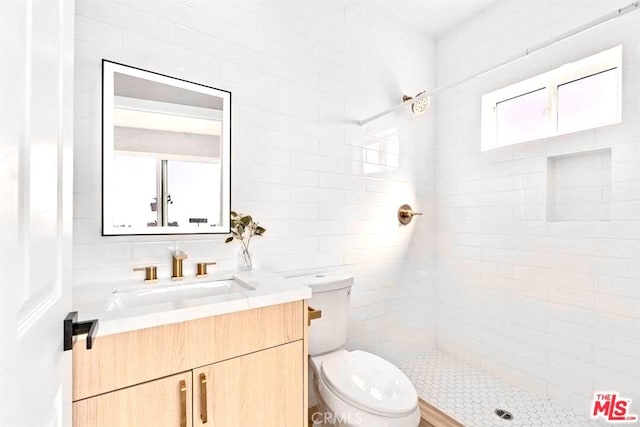 bathroom featuring a tile shower, vanity, tile walls, and toilet