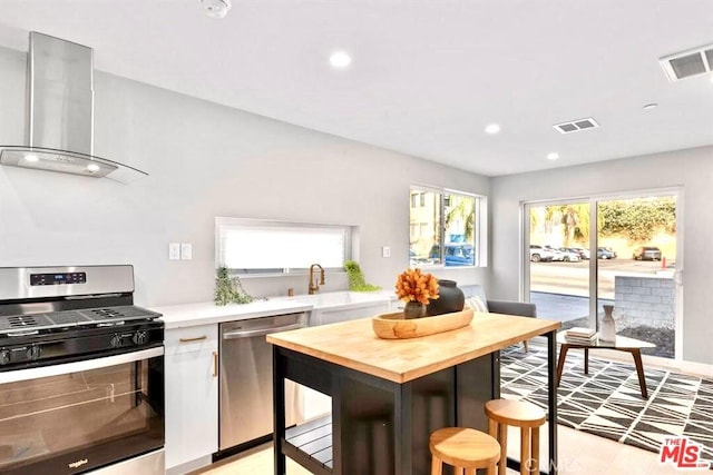 kitchen featuring stainless steel appliances, butcher block countertops, plenty of natural light, and wall chimney exhaust hood