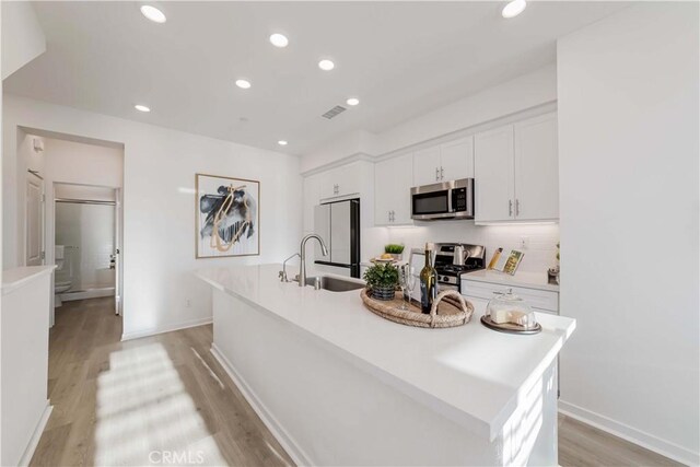 kitchen featuring white cabinetry, stainless steel appliances, an island with sink, sink, and light hardwood / wood-style flooring