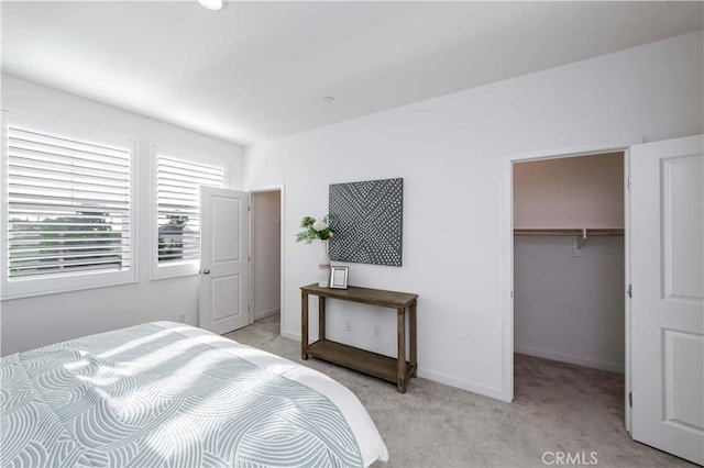 bedroom with light carpet, a spacious closet, baseboards, and a closet