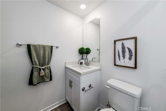 bathroom with toilet, wood finished floors, vanity, and baseboards