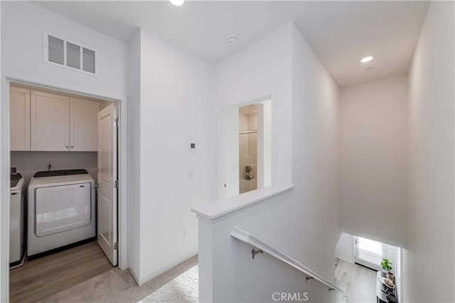 washroom with light carpet, washer and dryer, and cabinets