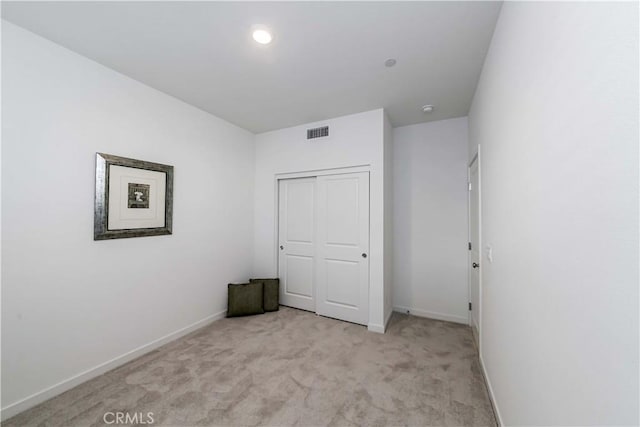 unfurnished bedroom with light colored carpet, a closet, visible vents, and baseboards