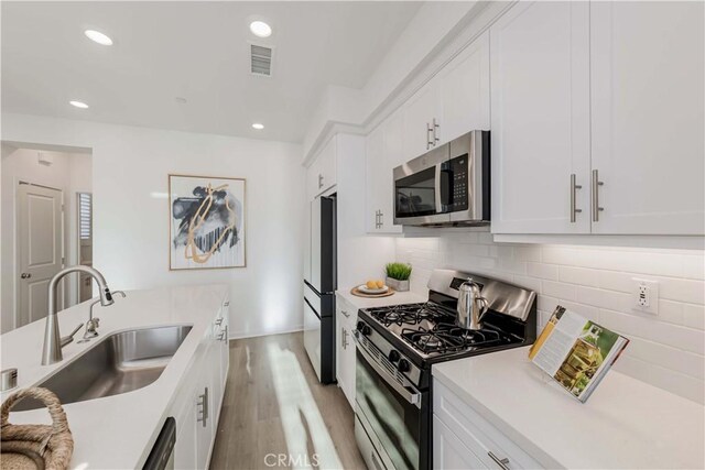 kitchen with appliances with stainless steel finishes, white cabinetry, decorative backsplash, sink, and light wood-type flooring