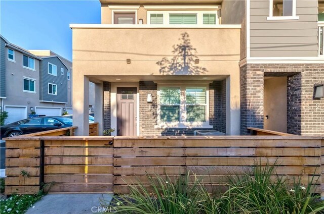 view of front of property with brick siding, fence, a balcony, and stucco siding