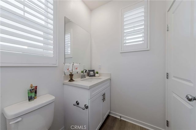 half bathroom with baseboards, vanity, toilet, and wood finished floors