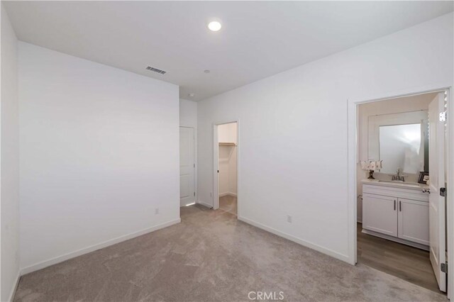 unfurnished bedroom featuring a spacious closet, light carpet, connected bathroom, a closet, and sink