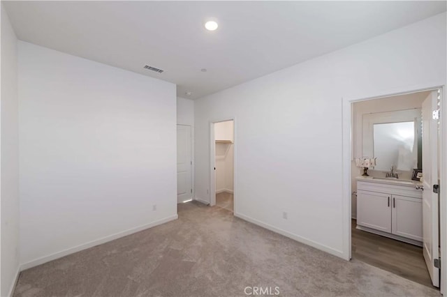 unfurnished bedroom featuring visible vents, ensuite bathroom, light carpet, a sink, and baseboards