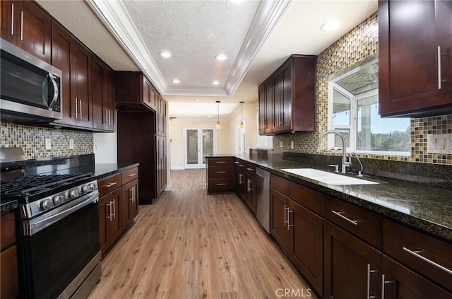 kitchen featuring dark stone counters, stainless steel appliances, a raised ceiling, decorative light fixtures, and light hardwood / wood-style flooring