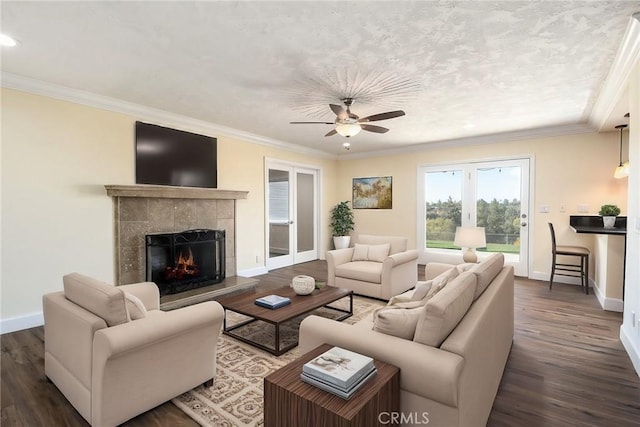 living room with ceiling fan, crown molding, dark wood-type flooring, and a tiled fireplace