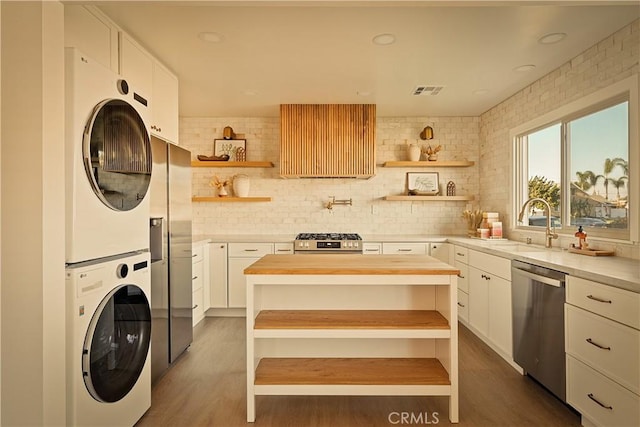 kitchen featuring stacked washer and dryer, sink, butcher block countertops, stainless steel appliances, and white cabinets