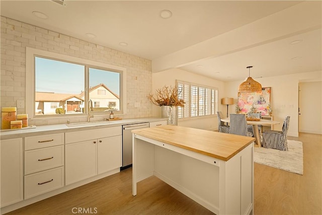 kitchen with sink, white cabinetry, hanging light fixtures, a kitchen island, and stainless steel dishwasher