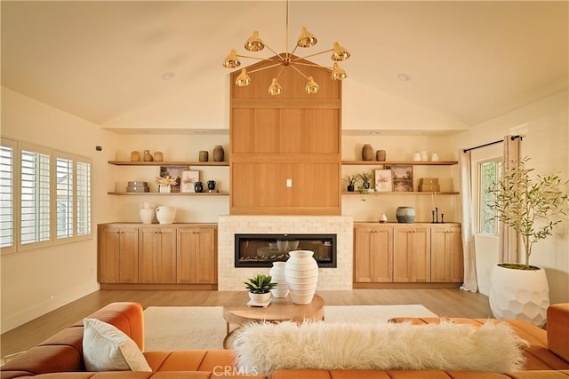 living room featuring a tiled fireplace, built in shelves, high vaulted ceiling, and light wood-type flooring