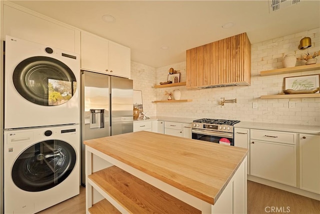 kitchen featuring stacked washer and dryer, stainless steel appliances, and white cabinets