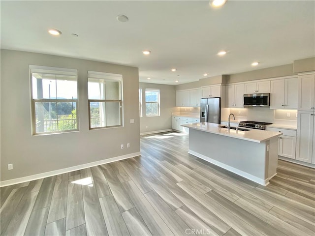 kitchen with a center island with sink, sink, light hardwood / wood-style flooring, appliances with stainless steel finishes, and white cabinetry