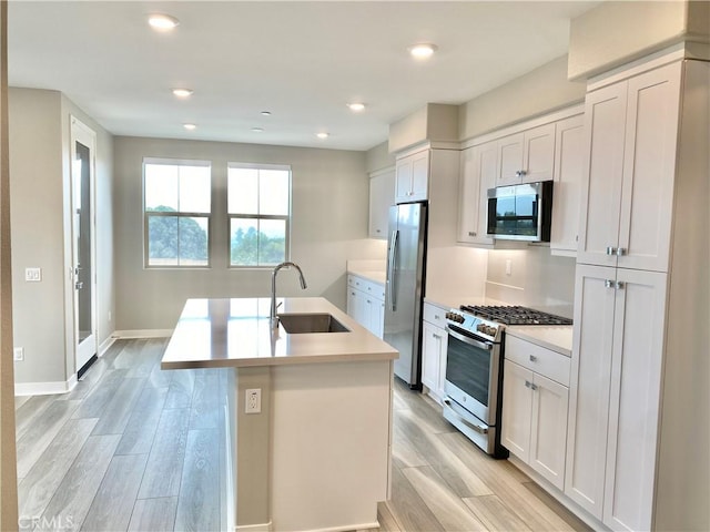 kitchen with a center island with sink, sink, light wood-type flooring, white cabinetry, and stainless steel appliances