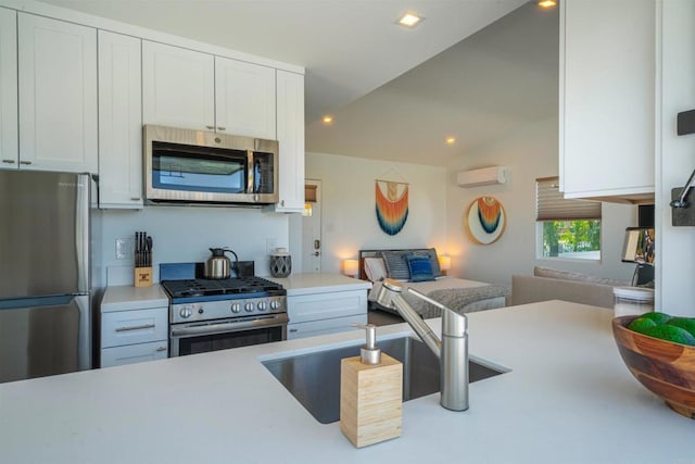 kitchen with sink, a wall mounted air conditioner, lofted ceiling, white cabinets, and appliances with stainless steel finishes