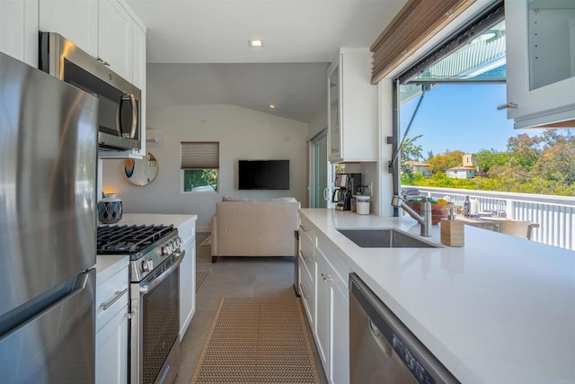 kitchen with sink, vaulted ceiling, white cabinets, dark tile patterned flooring, and appliances with stainless steel finishes